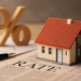 Miniatura di una casa su giornale finanziario con penna e simbolo percentuale in legno sullo sfondo per rappresentare i mutui 2025