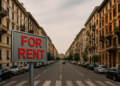 Cartello For Rent in primo piano su strada urbana con palazzi residenziali – simbolo del calo della domanda di affitti nelle città italiane nel 2025
