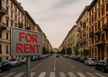 Cartello For Rent in primo piano su strada urbana con palazzi residenziali – simbolo del calo della domanda di affitti nelle città italiane nel 2025