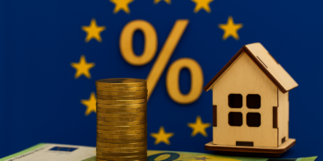 Moneta da un euro, casa in miniatura e bandiera UE con simbolo percentuale – concetto di taglio tassi BCE giugno 2025