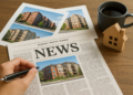 Tavolo con giornale aperto, foto di edifici residenziali, modellino di casa e tazza di caffè – simbolo della rassegna stampa con le notizie immobiliari