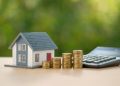 Modellino di casa, pile di monete crescenti e calcolatrice su sfondo verde: concetto di mutui casa e risparmio nel 2025