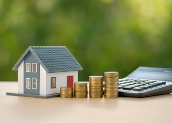 Modellino di casa, pile di monete crescenti e calcolatrice su sfondo verde: concetto di mutui casa e risparmio nel 2025