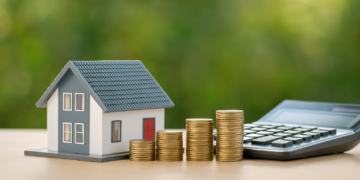Modellino di casa, pile di monete crescenti e calcolatrice su sfondo verde: concetto di mutui casa e risparmio nel 2025