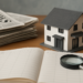 Notizie immobiliari rappresentate da modellino di casa, giornali, planner e lente d'ingrandimento su tavolo di legno