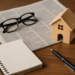 Modello di casa in legno, giornale, taccuino e occhiali su scrivania: concetto di notizie immobiliari