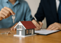 Due persone firmano un contratto immobiliare con un modellino di casa e chiavi sul tavolo, concetto legato al decreto Salva Casa