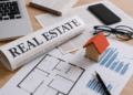 Scrivania con giornale, laptop e modello di casa in legno per notizie immobiliari settimanali