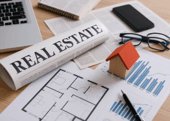 Scrivania con giornale, laptop e modello di casa in legno per notizie immobiliari settimanali