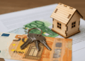 Modellino di casa in legno con chiavi e banconote in euro su documenti fiscali - IMU 2025