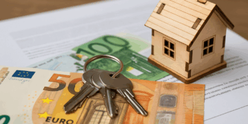 Modellino di casa in legno con chiavi e banconote in euro su documenti fiscali - IMU 2025