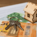 Modellino di casa in legno con chiavi e banconote in euro su documenti fiscali - IMU 2025