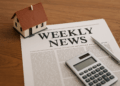 Modellino di casa, calcolatrice e giornale su scrivania: rassegna settimanale notizie immobiliari