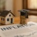 Miniatura di casa accanto a pila di monete con cappello accademico, simbolo di inflazione affitti 2025